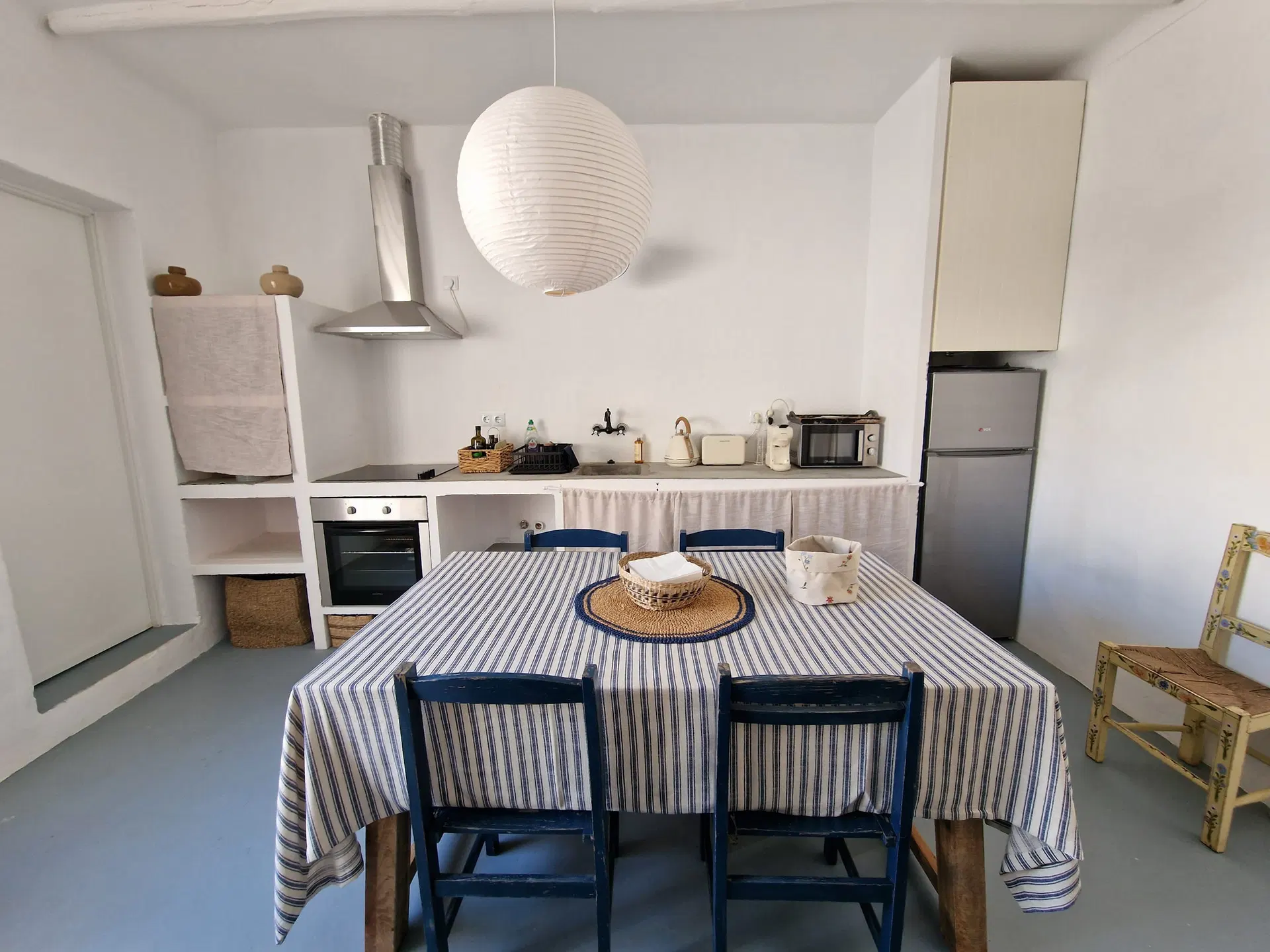 Mesa posta com toalha de riscas azuis na cozinha, com exaustor, forno e candeeiro de papel por cima.